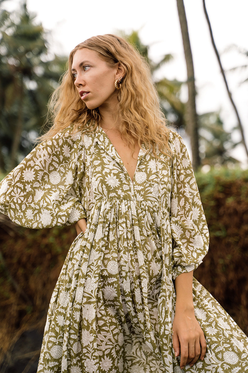 Daughters of India Kyra Midi Dress in Olive — upper body on beach with palms, V-neckline, billowed sleeves