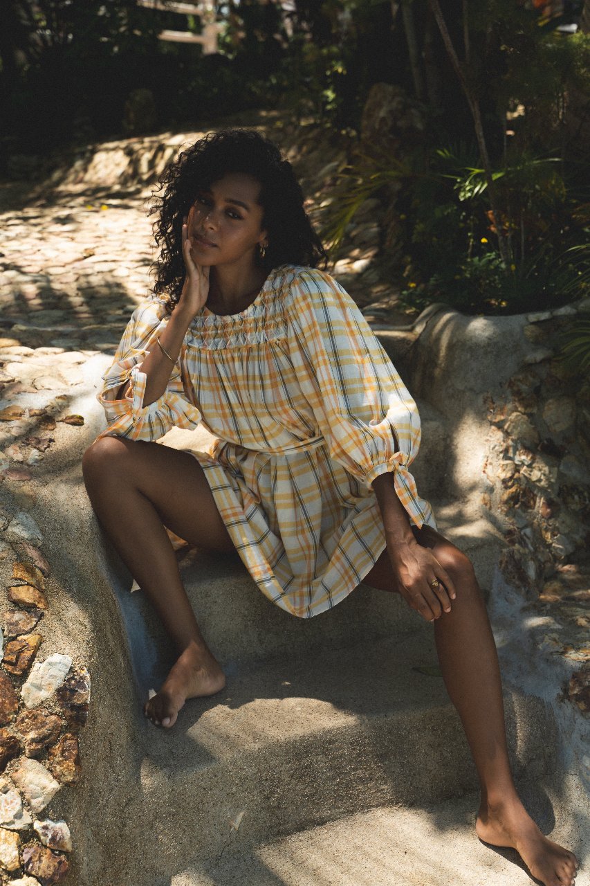 Freya Dress Honeycomb Plaid — seated on stone steps in dappled sunlight, relaxed candid pose, handloom woven honeycomb yellow plaid with embroidered detail, boho ethical artisan dress | Daughters of India