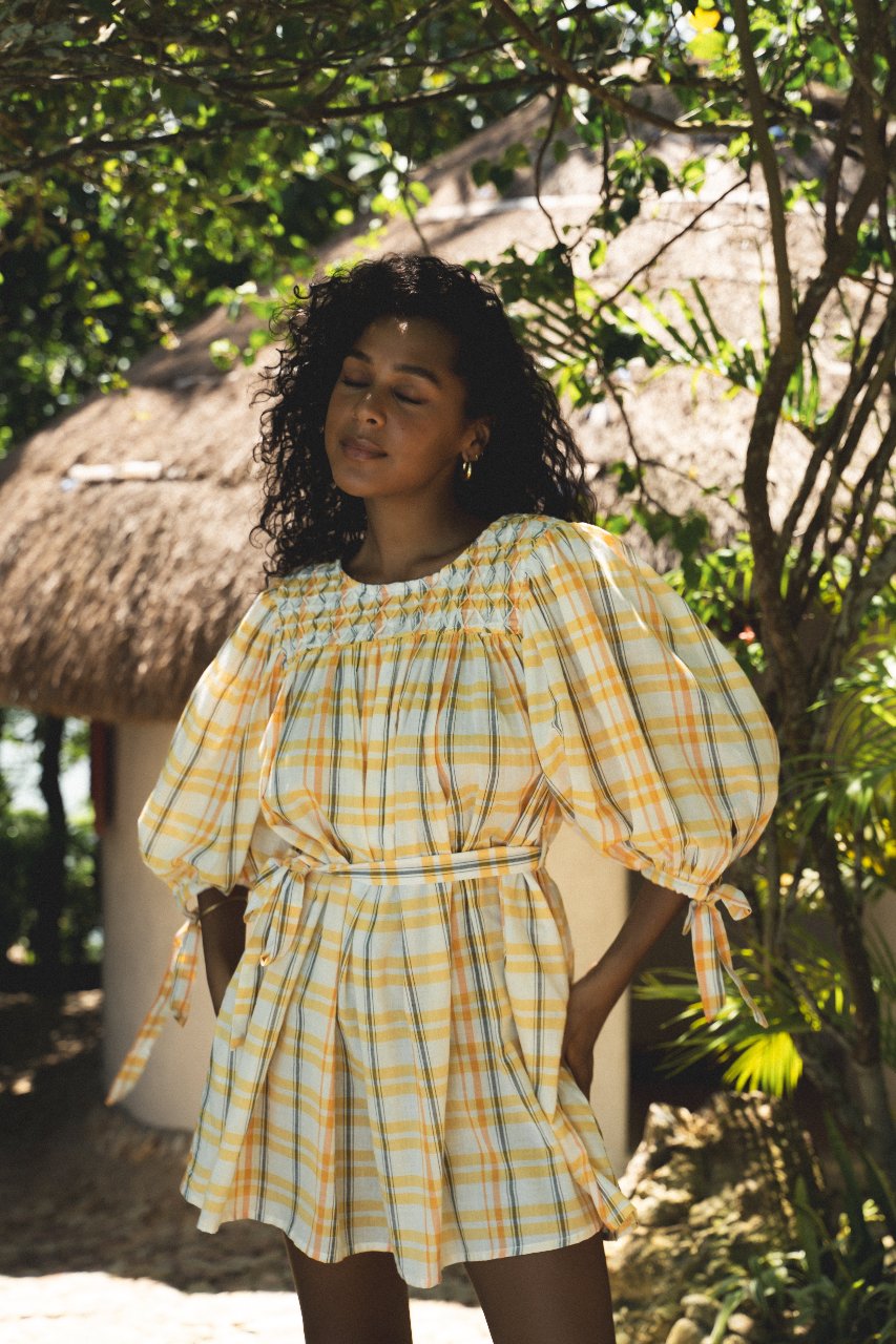 Freya Dress Honeycomb Plaid — garden lifestyle shot by thatched hut, front portrait, showing embroidered neckline panel and waist belt, handloom woven honeycomb plaid, boho artisan mini dress | Daughters of India