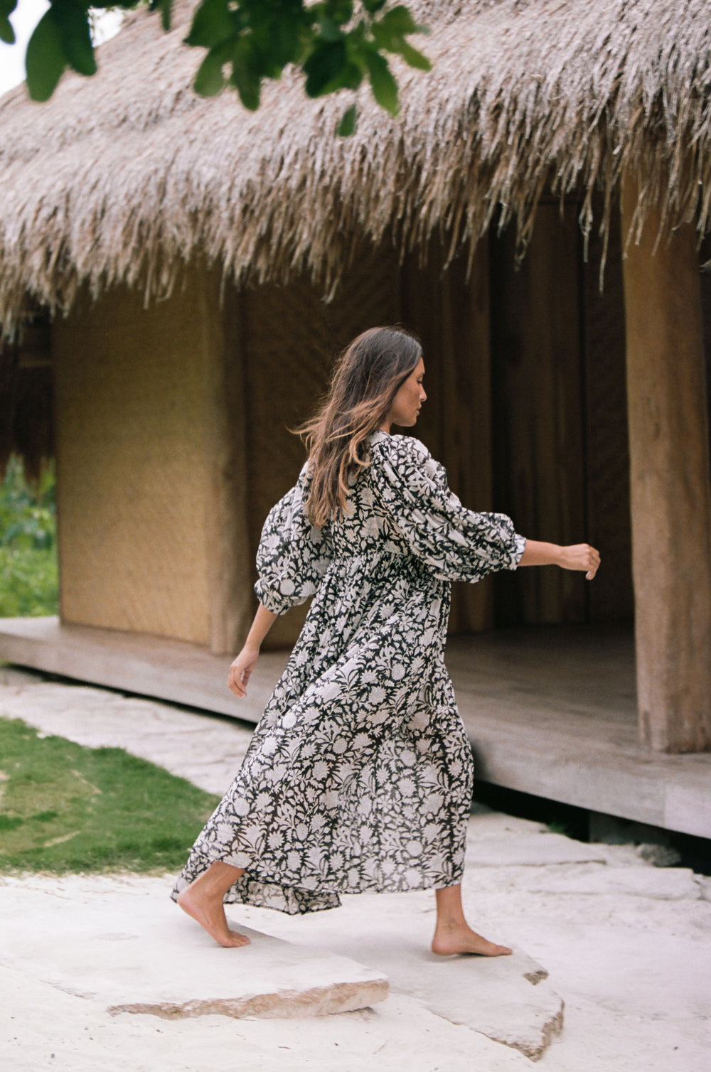Daughters of India Kyra Maxi Dress in Pepper — back view walking past thatched hut, billowed sleeves, gathered waist